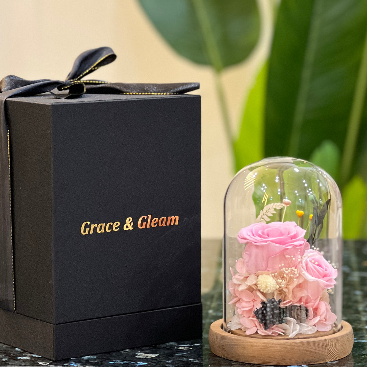 Pink forever flowers dome beside a Grace & Gleam gift box