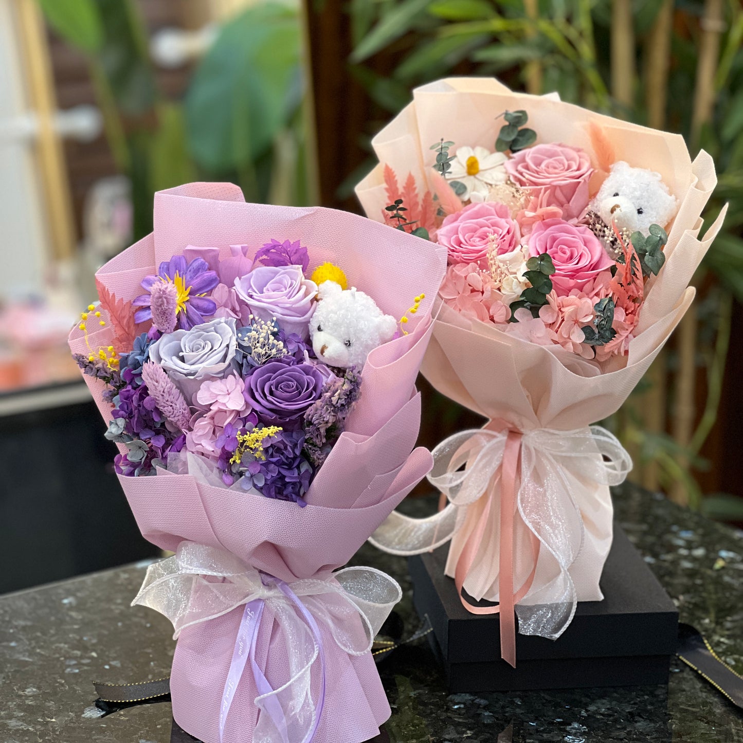 Purple and pink preserved flower bouquets with teddy bears, shown side by side