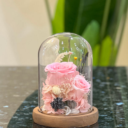 Front view of preserved pink roses, hydrangea and dried flowers in a glass dome