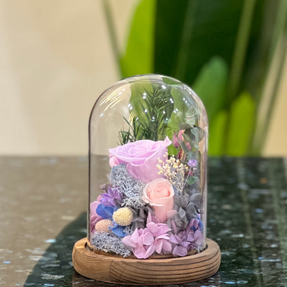 Side view of a preserved purple rose garden in a tall glass dome on a wooden base