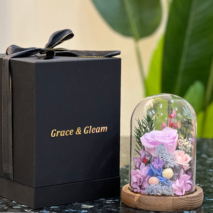 Purple forever flowers dome - preserved lavender rose and hydrangea under a glass dome beside a Grace & Gleam gift box