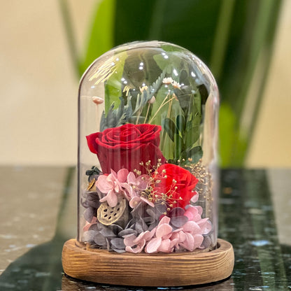 Front view of preserved red roses, pink hydrangea and dried flowers in a glass dome