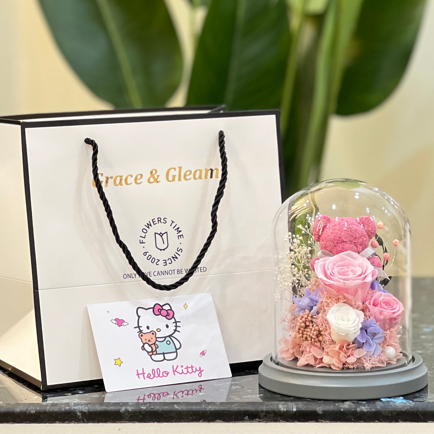 Pink rose bear in a glass dome beside a Grace & Gleam gift bag