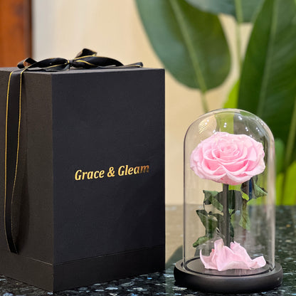 Pink forever rose in a glass dome beside a Grace & Gleam gift box