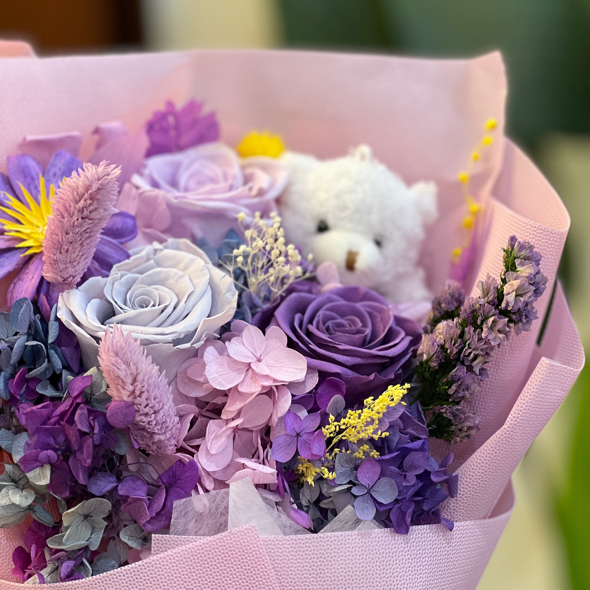 Preserved purple roses, hydrangea and dried flowers with a small white bear